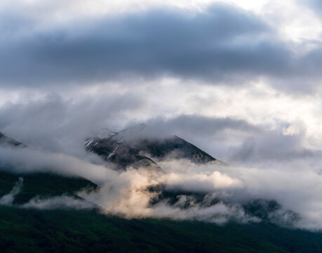 First rays of morning sun light rain clouds and mountain tops along Alsek River