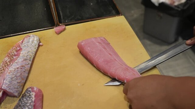 Close-up of a chef filleting fresh fish with a sharp knife on a cutting board, professional seafood preparation in a commercial kitchen, culinary process footage.