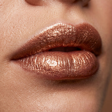 Close-up of female lips wearing shimmering metallic bronze lipstick with a glitter finish, showcasing professional beauty makeup and skin texture