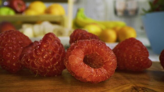Tracking, extra closeup shot across tiny raspberries on cutting board in kitchen