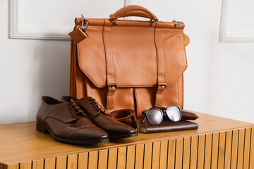 Brown leather briefcase with mens dress shoes, belt, and eyeglasses on a wooden cabinet, business...