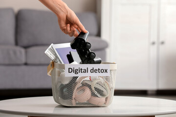 Young woman putting game pad into basket with different devices and text DIGITAL DETOX at home, closeup © Pixel-Shot