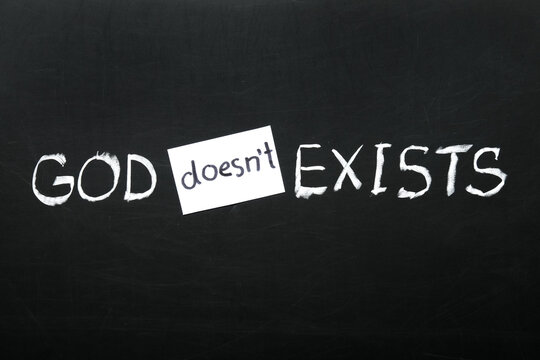 God doesnt exists written in chalk on a blackboard with a paper note, atheism and belief concept, the word "doesnt" is on a small white paper note covering the original word