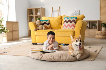 Fototapeta premium Little happy Asian boy reading book with cute Corgi dog at home