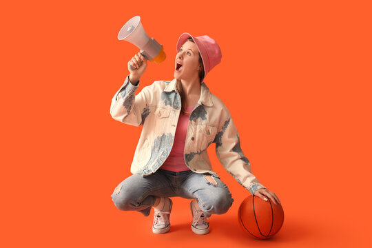 Young woman with ball shouting into megaphone on red background