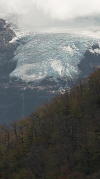 Casta&ntilde;o Overo Glacier with icy textures on the mountain slope, framed by temperate forest with autumn foliage in Los Glaciares National Park, Argentina.