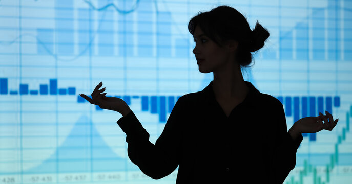 Businesswoman silhouette presenting financial data and market analysis on a blue digital screen with Charts and graphs, Charts and graphs illustrate economic trends and investment strategies