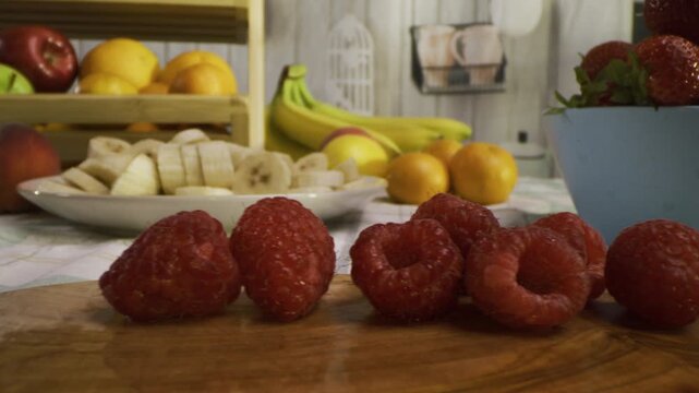 Tracking shot across raspberries on cutting board with other surrounding fruit