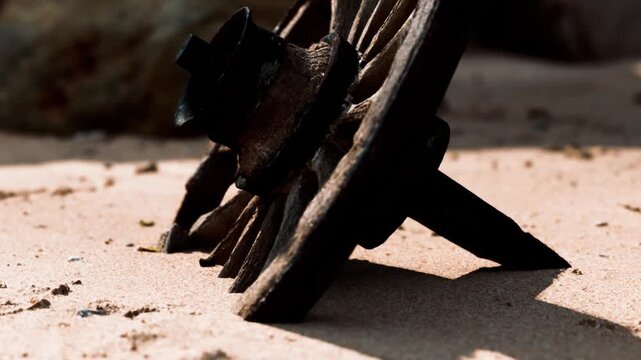 A rusty object is placed on the sand near some rocky formations at the beach. Sunlight casts shadows, showing the texture and details of the metal. The scene captures the beach environment.