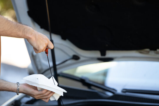 Close-up of a man's hands checking the oil dipstick of a car engine, illustrating routine car maintenance and vehicle care