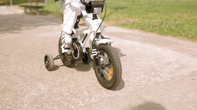 Young child learning to ride bicycle with training wheels in park