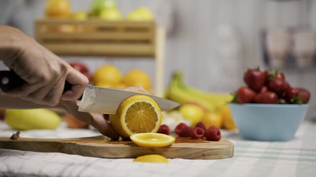 Medium shot of person using knife to slice through orange on counter with other fruit around