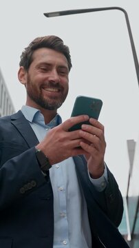 Excited Caucasian business man smiling read good news message smartphone outdoor happy positive male sms businessman entrepreneur employer work looking at mobile phone screen in city winning success