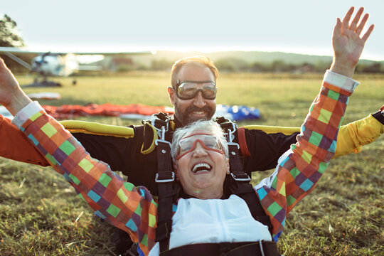 Senior woman and instructor celebrating tandem skydive landing at airfield