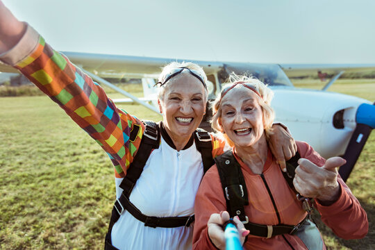 Two senior women taking selfie in skydiving gear at airfield