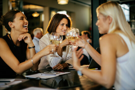 Three businesswomen toasting with white wine at a bar