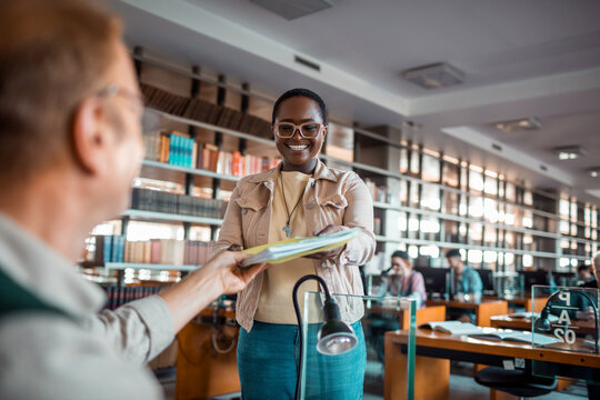 Student handing documents to librarian in university library