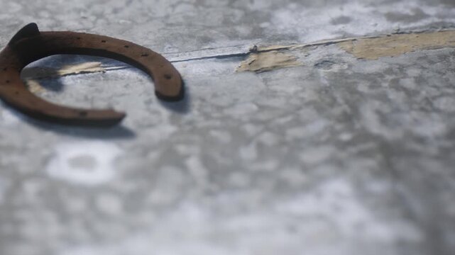 A horseshoe is placed on an old, worn wooden floor. The barn gives a rustic look. Light falls softly on the horseshoe, revealing its shape and texture.