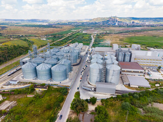 Industrial area with large storage silos and buildings near a rural road surrounded by green fields and distant hills © DSMT