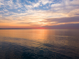 Obraz premium Sunset over calm water at the shoreline with clouds and color