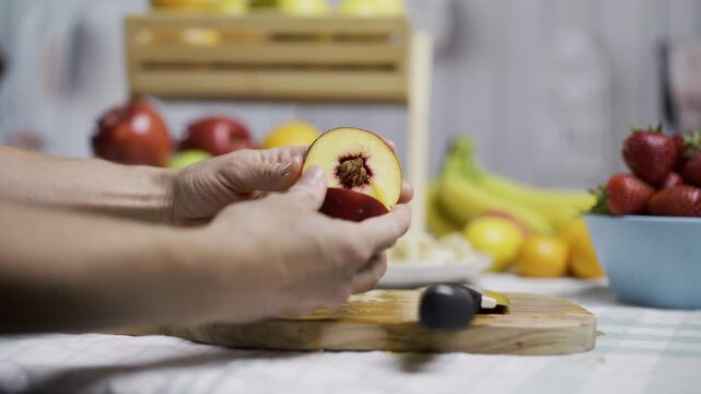 Woman cutting open peach and slicing it up in kitchen with other surrounding fruit, closeup shot