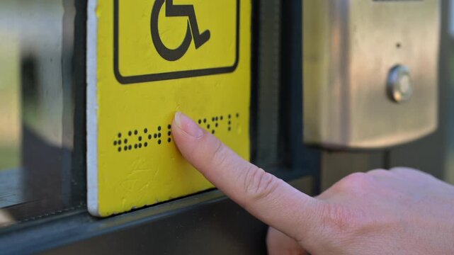 A blind woman reads the braille sign next to a call button.