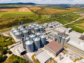 Large grain storage facility located in rural area with several silos and access roads surrounded by fields and hills under a clear sky © DSMT
