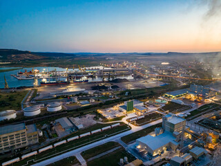 Fototapeta premium Shipping port at dusk with loading and unloading activities taking place as cranes and ships work together along the coast