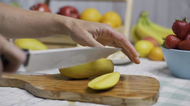 Female chef using knife to cut up juicy mango in kitchen - closeup