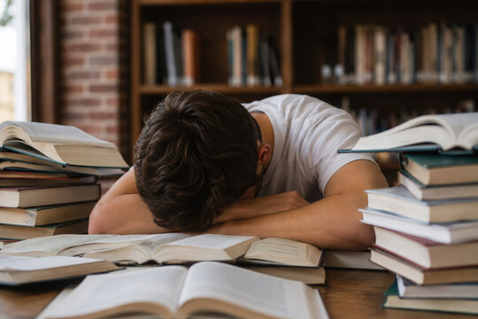 Tired teenage boy with books at table in library