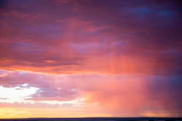 Fototapeta premium Vibrant pink and purple sunset sky filled with dramatic storm clouds and a glowing backlit rain curtain background