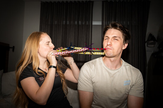 Two Adults Blowing Party Horns Indoors During Home Celebration