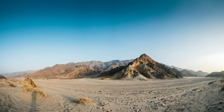 A wide panoramic view of a vast desert landscape with sandy ground and rocky mountains under a clear blue sky during the bright daylight hours