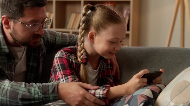 Sad Caucasian male father touching little girl daughter playing game smartphone man schoolgirl kid ignore dad child using mobile phone at home guy parent family problem talk gadget virtual addiction