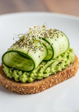 Freshly sliced green cucumber rounds layered over smashed ripe avocado on toasted whole grain bread, garnished with seeds and sprouts, pepper, homemade, brunch