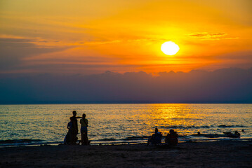 Fototapeta premium Sauble Beach, Canada - May 8 2026: Golden sunlight reflects off gentle lake waves and soft sands as the sun sets over the scenic horizon of Sauble Beach
