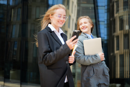 Business women share a moment of joy outside a modern office building while using their devices