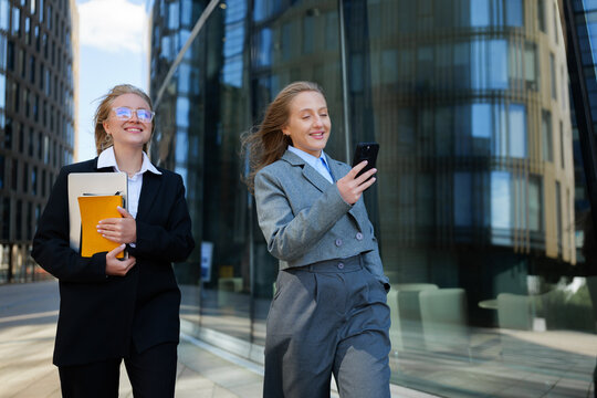 Two professionals enjoying a sunny day while walking and checking their phones in a modern cityscape