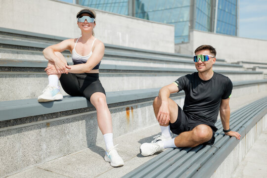 Stylish athletes relax on outdoor steps under bright blue sky during sunny afternoon workout session