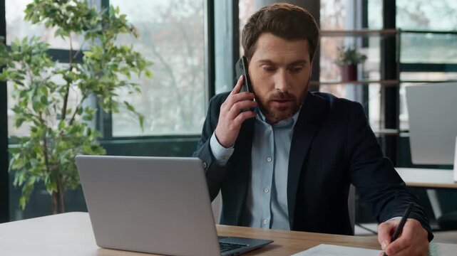 Busy Caucasian businessman talking mobile phone working laptop in office arguing client conflict multitasking angry male business man manager consultant entrepreneur writing notes stressed guy indoor