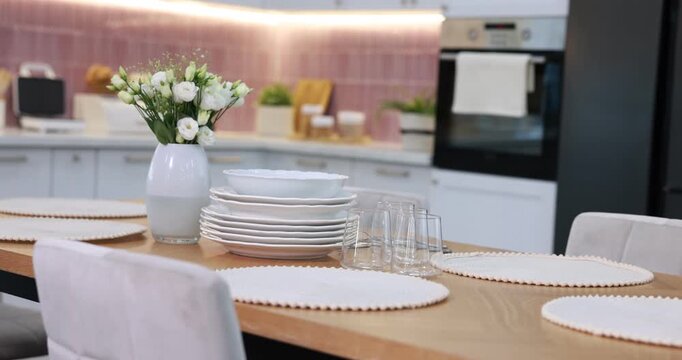 Stylish setting with vase of flowers, plates and glasses on wooden table in kitchen. Camera moving