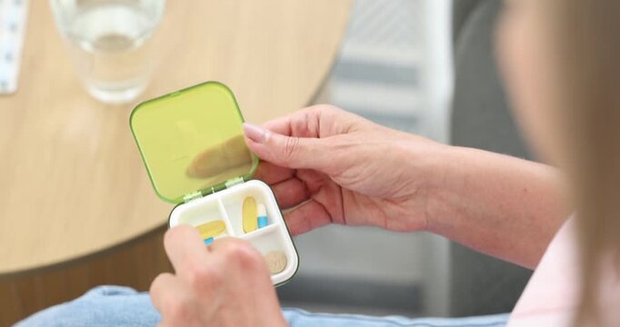 Senior woman taking pill from organizer at home, closeup