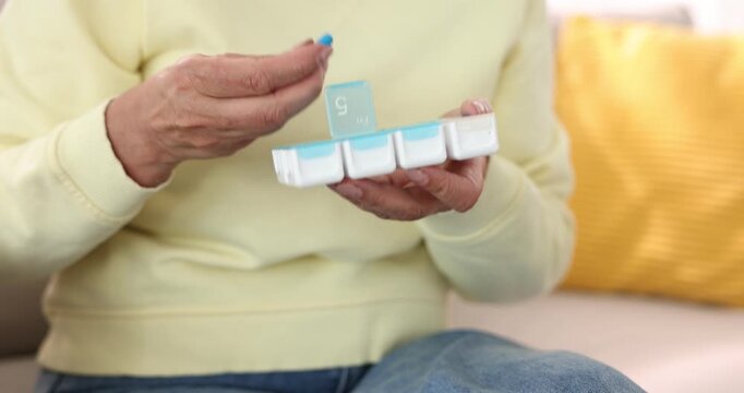 Senior woman taking pill out of organizer at home, closeup. Camera moving in