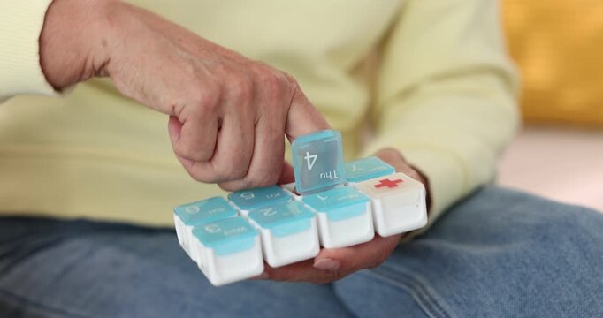 Senior woman taking pill out of organizer at home, closeup. Camera moving in