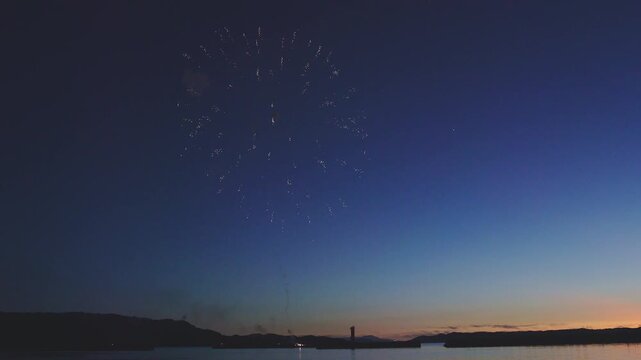 沿岸の夕暮れの深い青空に弾けるキラキラとした打ち上げ花火