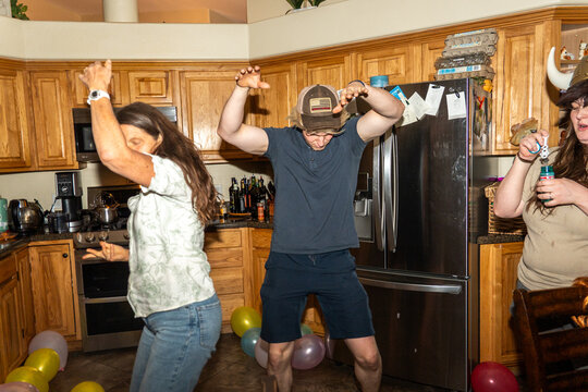 Friends dancing in busy kitchen during lively home celebration with balloons