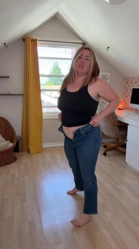 woman has a hard time putting on a pair of blue jeans