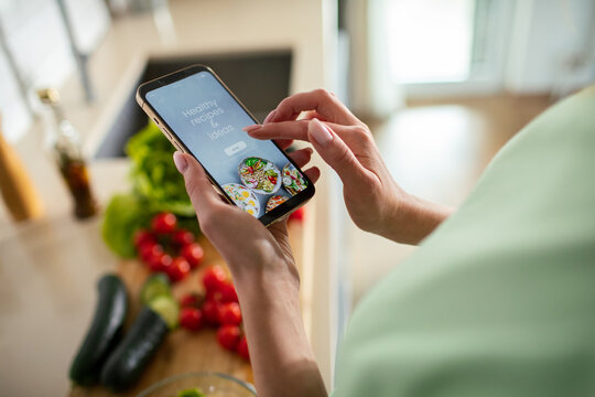Woman using recipe app on smartphone in home kitchen