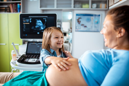 Smiling daughter with pregnant mother during ultrasound exam in clinic