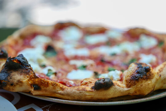 Close‑up of a freshly baked margherita pizza with golden crust, melted mozzarella, and basil leaves on a metal plate.